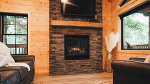 Una sala de estar acogedora con chimenea de piedra, sofás de cuero y un ventanal con vistas a árboles.