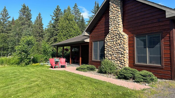A log cabin with a stone chimney, a covered porch, and a well-maintained lawn. - Lodge-Style Northwoods Home Permit: TBES-BBSMJP (Poplar)