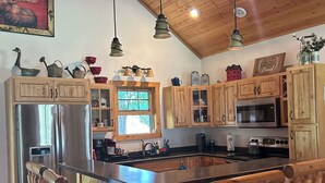 A kitchen with wooden cabinets, a central island with stools, a refrigerator, and a microwave. - Lodge-Style Northwoods Home Permit: TBES-BBSMJP (Poplar)