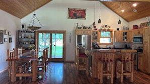 A spacious kitchen with wooden cabinets, a central island, and a dining area with wooden chairs. - Lodge-Style Northwoods Home Permit: TBES-BBSMJP (Poplar)