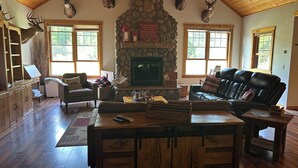 A cozy living room with a stone fireplace, leather sofas, and mounted deer heads. - Lodge-Style Northwoods Home Permit: TBES-BBSMJP (Poplar)