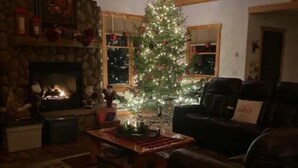 A cozy living room with a fireplace, a Christmas tree, and a stone wall. - Lodge-Style Northwoods Home Permit: TBES-BBSMJP (Poplar)