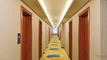 A hotel hallway with doors on both sides, a carpeted floor, and a ceiling light fixture.