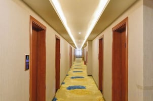 Pasillo de hotel con puertas a ambos lados, suelo alfombrado y una lámpara en el techo.