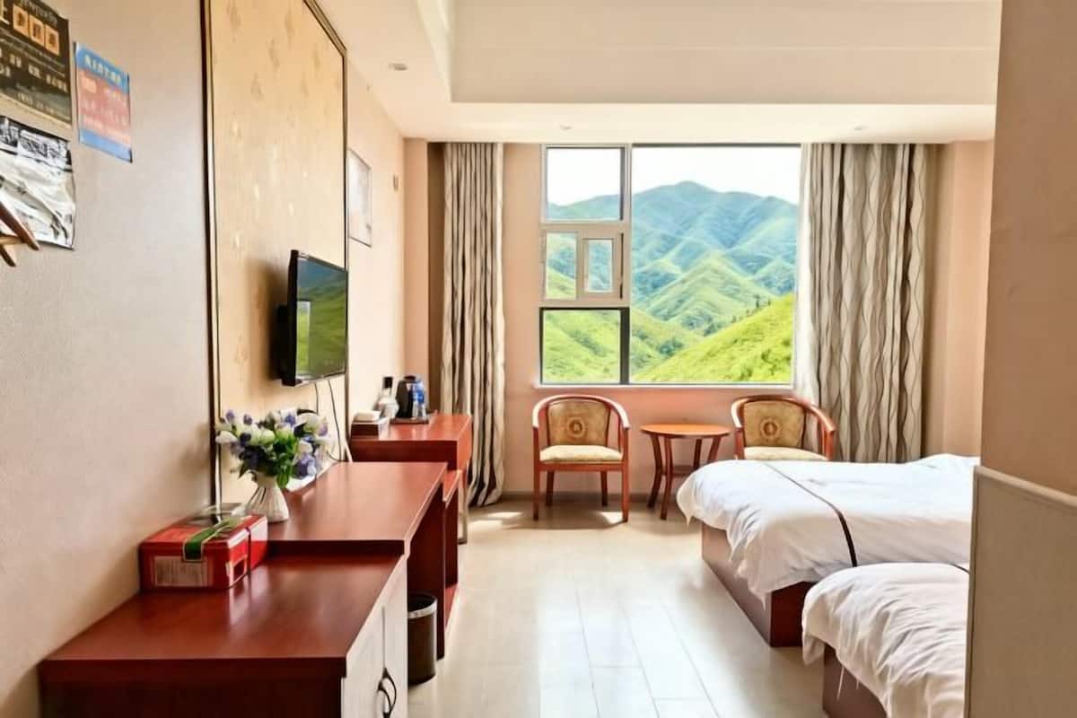 A hotel room with a bed, a desk, a chair, a TV, and a window with a mountain view.