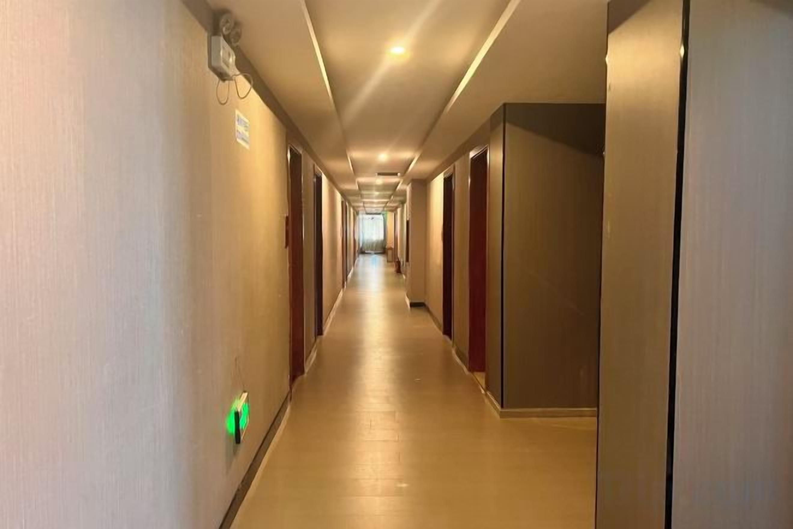 A hotel corridor with doors on both sides, a light switch on the wall, and a ceiling light.