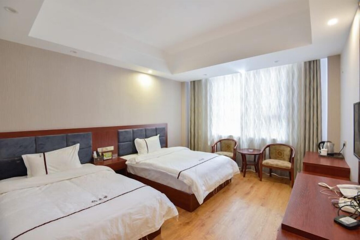 A hotel room with two beds, a desk, a chair, and a television.