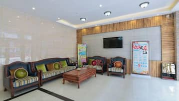 A hotel lobby with a reception desk, sofas, a coffee table, and a television screen.