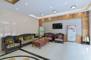 A hotel lobby with a reception desk, sofas, a coffee table, and a television screen.