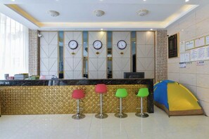 A reception area with a counter, four stools, a blue and yellow tent, and three clocks on the wall. - Daozhimeng Hotel (Daocheng County)