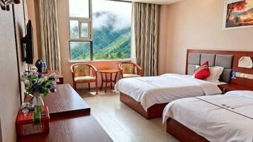 A hotel room with two beds, a desk, a chair, a small table, and a window with a mountain view.