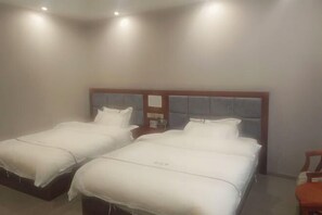 A hotel room with two single beds, a wooden headboard, a nightstand, and a chair. - Daozhimeng Hotel (Daocheng County)