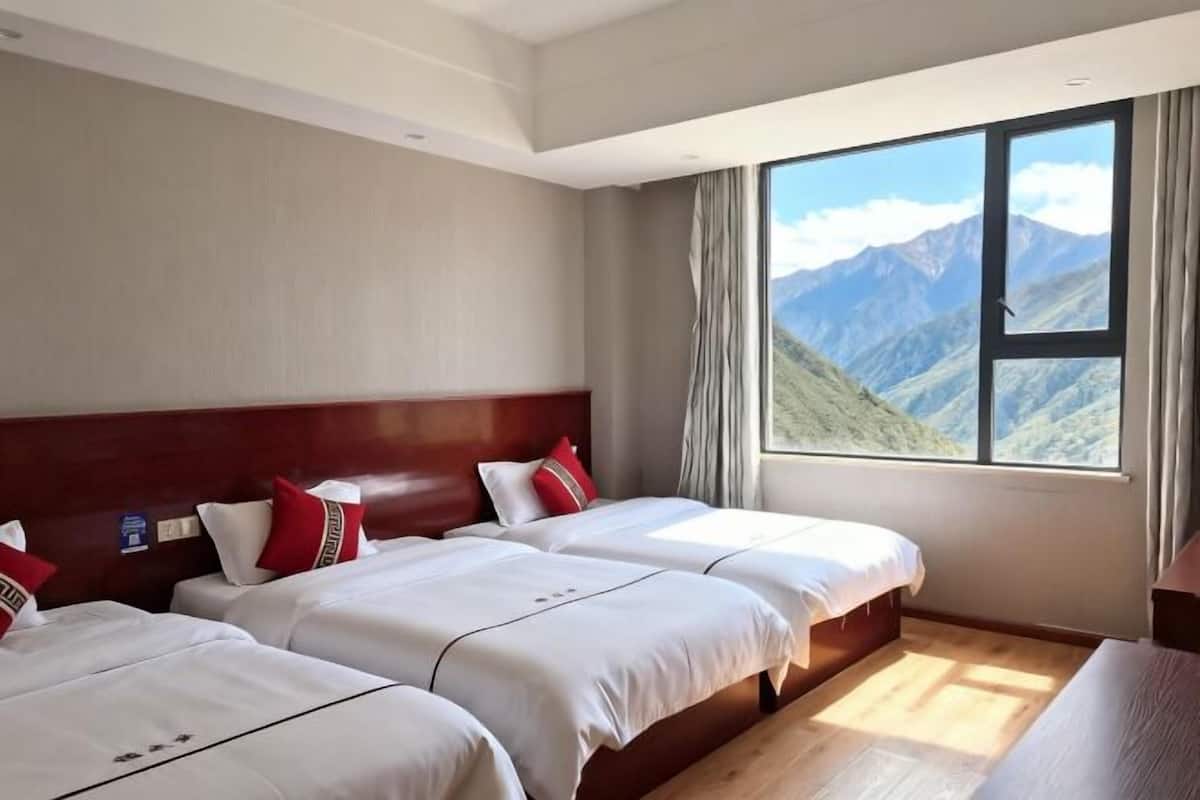 A hotel room with three beds, a wooden headboard, a large window with a mountain view, and a wooden floor.