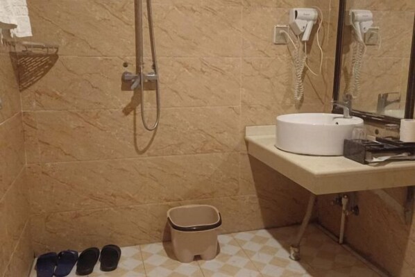 A bathroom with a marble wall, a sink, a mirror, a hairdryer, and a trash bin. - Daozhimeng Hotel (Daocheng County)