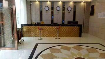 A hotel reception area with a reception desk, clocks, and a patterned floor.