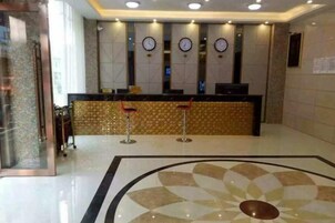 Zona de recepción de hotel con mostrador, relojes y suelo estampado.