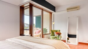 Une chambre avec un grand lit, une porte-fenêtre coulissante donnant sur un balcon, une chaise et un miroir.