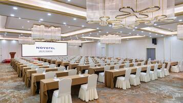 Un salón de conferencias con filas de mesas, una pantalla grande y candelabros.