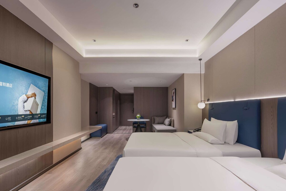 A modern hotel room with a large bed, a desk, a chair, a small table, and a television mounted on the wall.