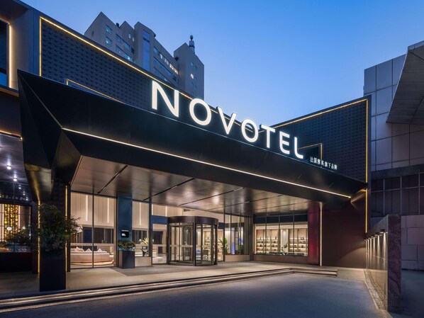 A hotel entrance with a prominent 'NOVOTEL' sign, glass doors, and a modern architectural design.