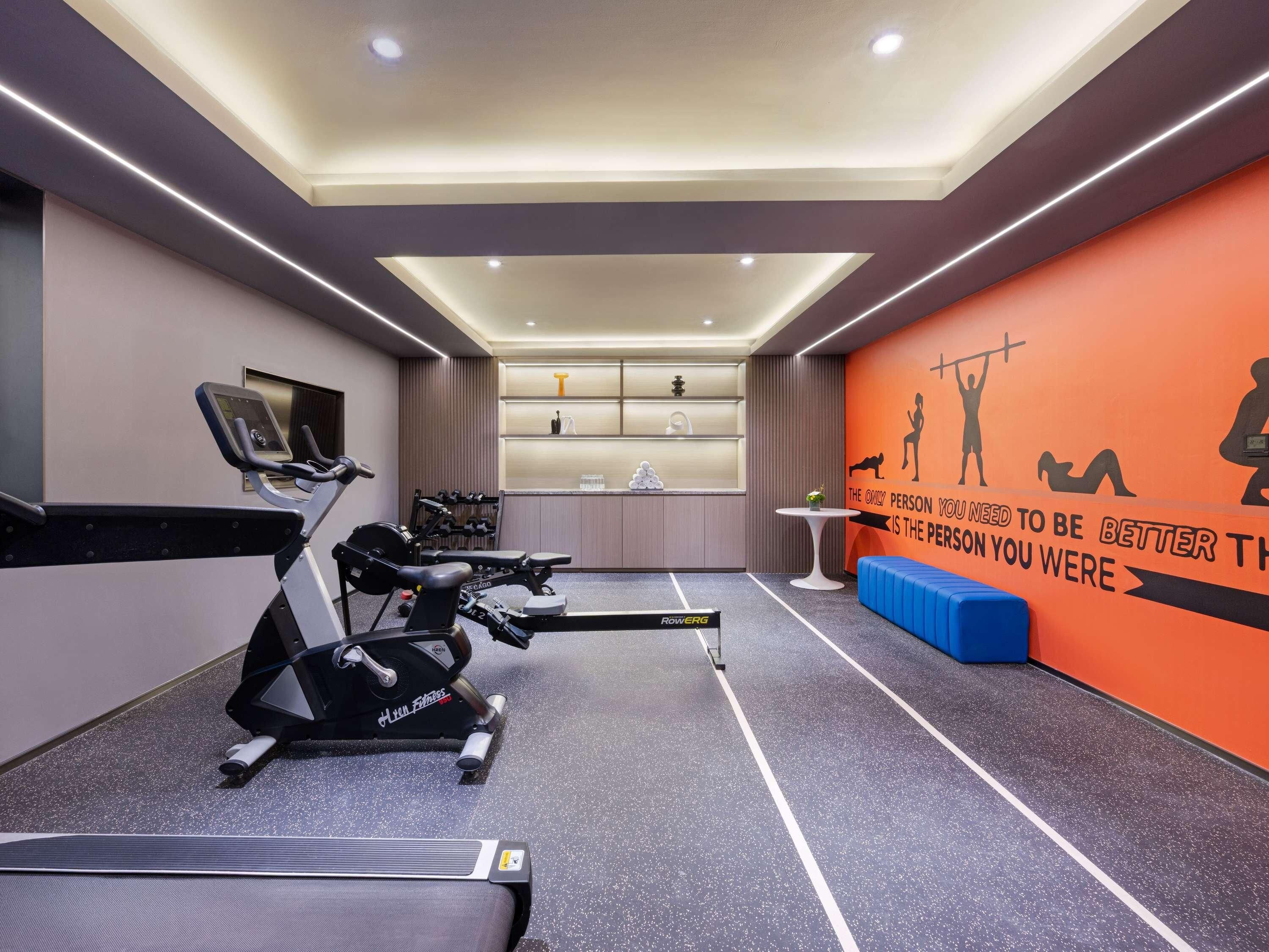 Un gimnasio con cintas de correr, una pared con siluetas de ejercicios y una frase motivadora.