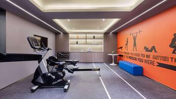 Un gimnasio con cintas de correr, una pared con siluetas de ejercicios y una frase motivadora.