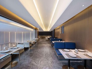 Un espace de restauration moderne dans un hôtel, avec de longues tables, des sièges rembourrés bleus et un sol en marbre.