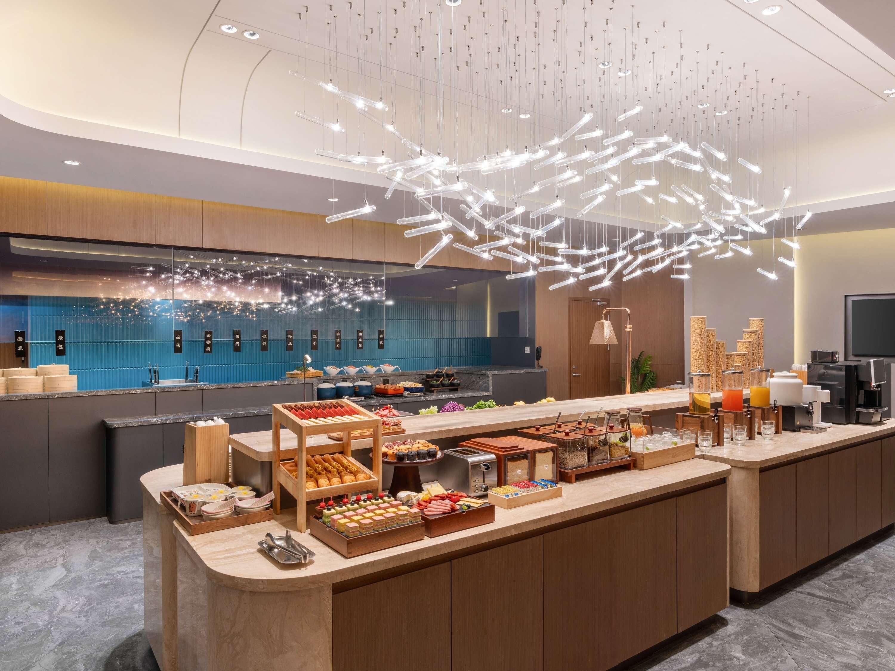 Un moderno vestíbulo de hotel con un mostrador central que exhibe diversos alimentos y una estación de café.