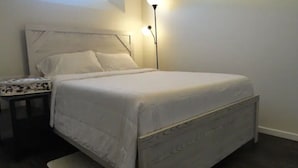 En pænt redt seng med sengegavl, et natbord med mønstret dug og en gulvlampe.
