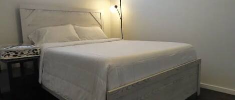 A neatly made bed with a headboard, a bedside table with a patterned cover, and a floor lamp.