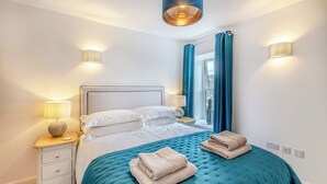 A neatly made bed with a teal bedspread and two folded towels, a bedside lamp, and a wall-mounted light fixture. - 2 bedroom accommodation in Casterton, near Kirkby Lonsdale (Casterton, near Kirkby Lonsdale)