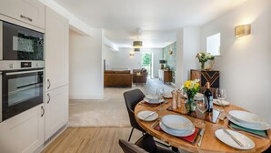 A modern kitchen with built-in appliances, a dining area with a wooden table set for four, and a view into the living room. - 2 bedroom accommodation in Casterton, near Kirkby Lonsdale (Casterton, near Kirkby Lonsdale)