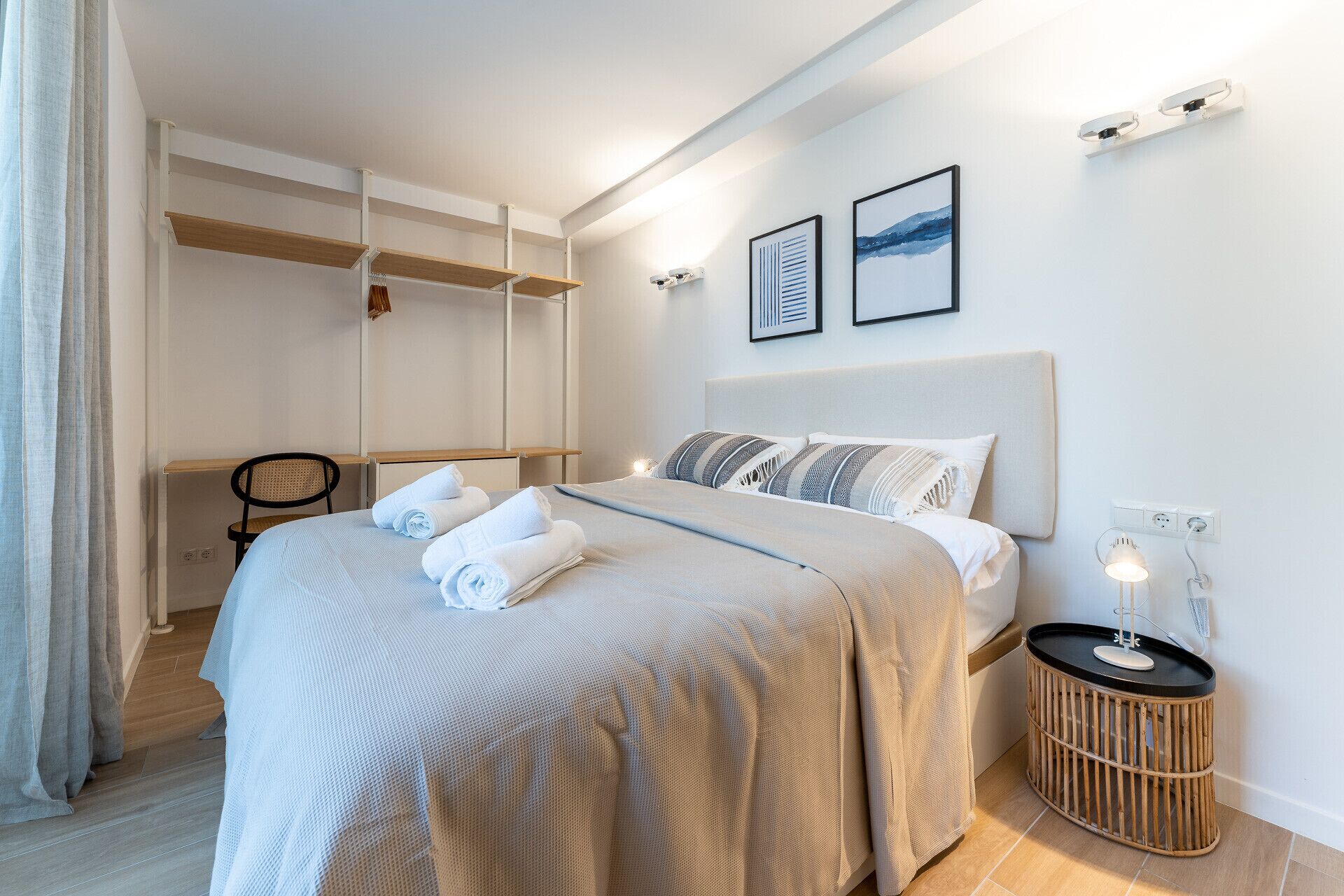 Una camera d'albergo moderna con un letto, una scrivania e una sedia. Due quadri appesi alla parete e un tavolino con una lampada.