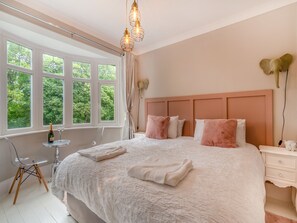 Une chambre à coucher avec un grand lit, une table de chevet, une chaise et une fenêtre avec des rideaux.
