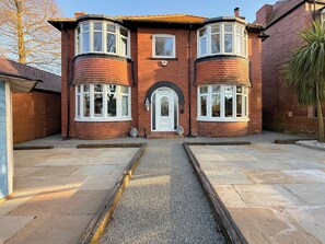 A two-story brick house with a central entrance, two bay windows, and a gravel driveway.