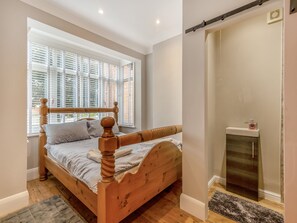 A wooden bed with a headboard, a window with blinds, a radiator, and a small rug on the floor.
