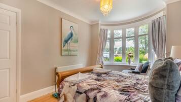 A bedroom with a bed, a window with curtains, a chandelier, and a painting of a bird.