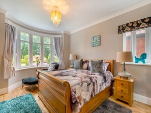 A bedroom with a wooden bed, two bedside tables with lamps, a window with curtains, a rug, and a decorative sign on the wall.