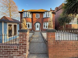 A brick house with a central entrance, two lion statues, and a gated driveway.