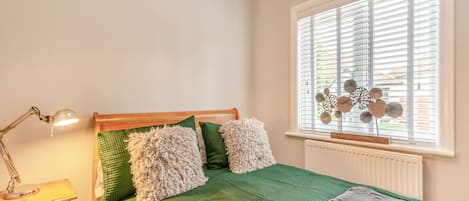 A bedroom with a bed, a nightstand, a lamp, and a window with blinds.