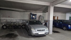 Un aparcamiento con un coche plateado estacionado en un lugar, pilares de hormigón y un coche azul al fondo.