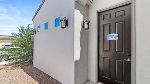 Un edificio con una puerta marrón oscuro, dos faroles fijados en la pared y un pequeño ventanal azul.