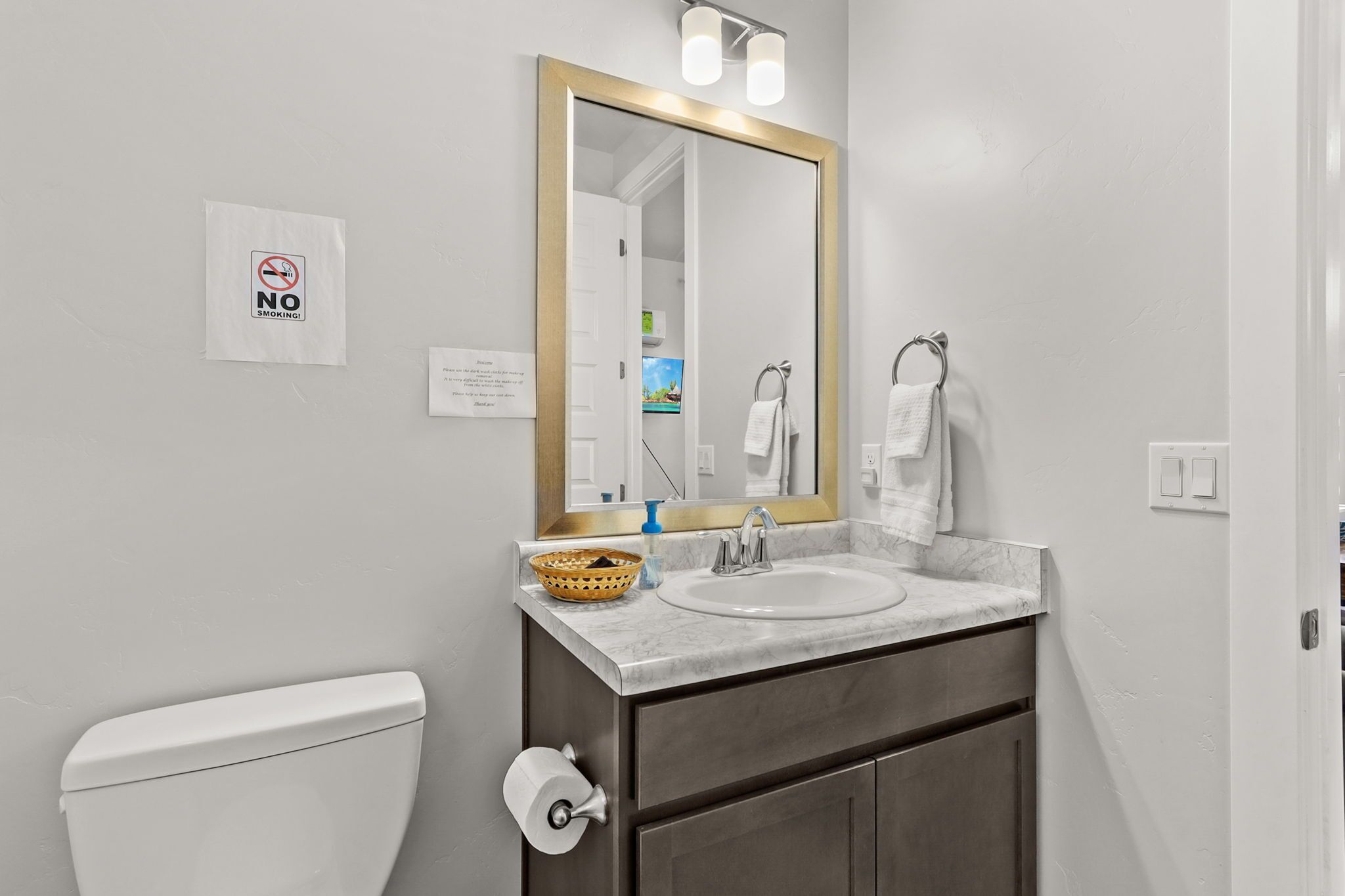 A bathroom with a white toilet, a sink with a marble countertop, a mirror with a gold frame, and a 'No Smoking' sign.