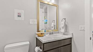 A bathroom with a white toilet, a sink with a marble countertop, a mirror with a gold frame, and a 'No Smoking' sign.