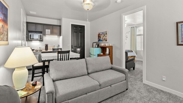 Sala de estar con un sofá gris, una mesa de comedor y una zona de cocina con microondas.