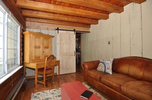 Una habitación acogedora con techo de madera, un sofá de cuero marrón, un escritorio de madera y una silla.