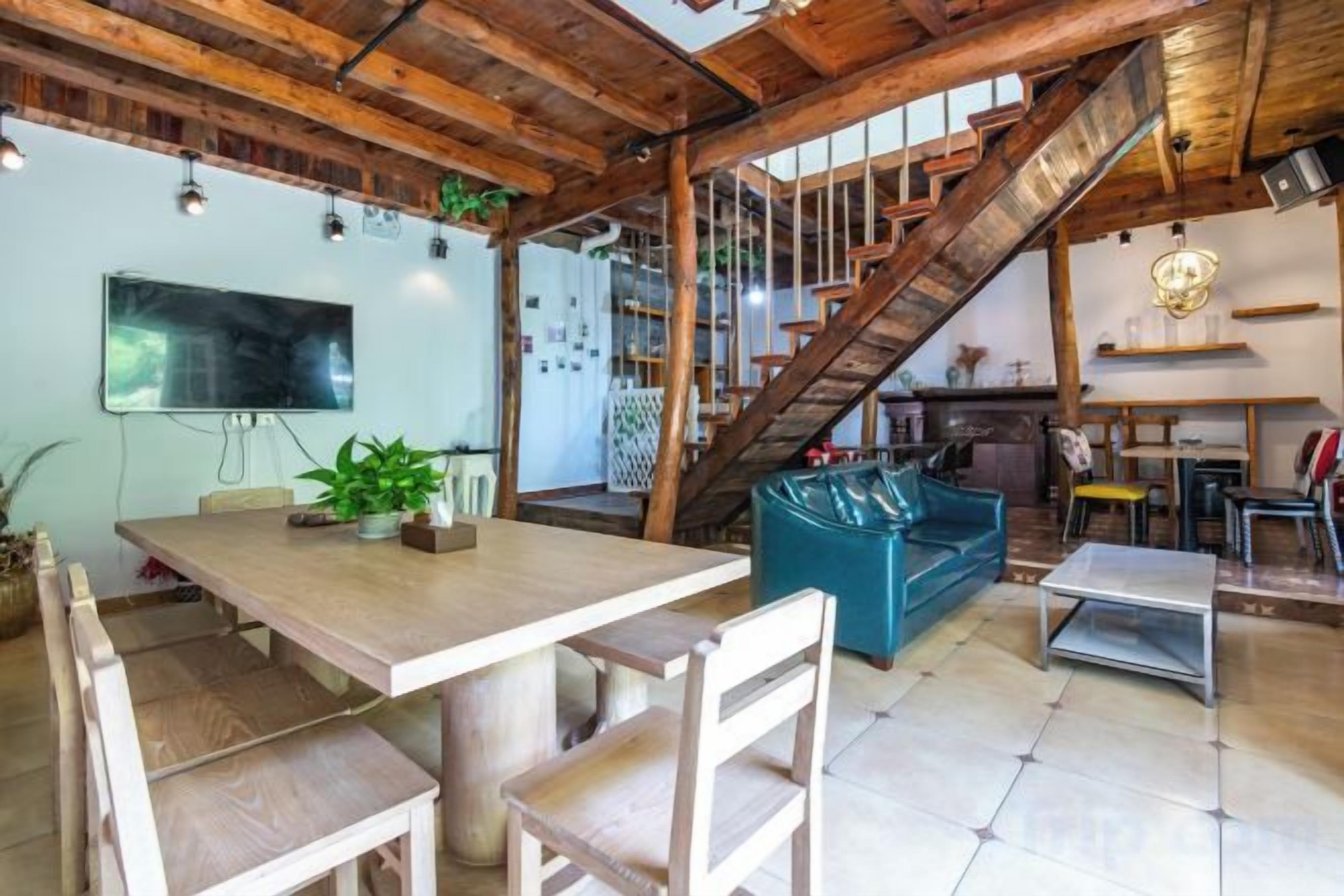 Un amplio salón con techo de madera, una escalera, un sofá y una mesa de comedor.