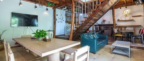 A spacious living area with a wooden ceiling, a staircase, a sofa, and a dining table.