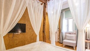 A bedroom with a bed, a TV mounted on the wall, and a window with curtains.