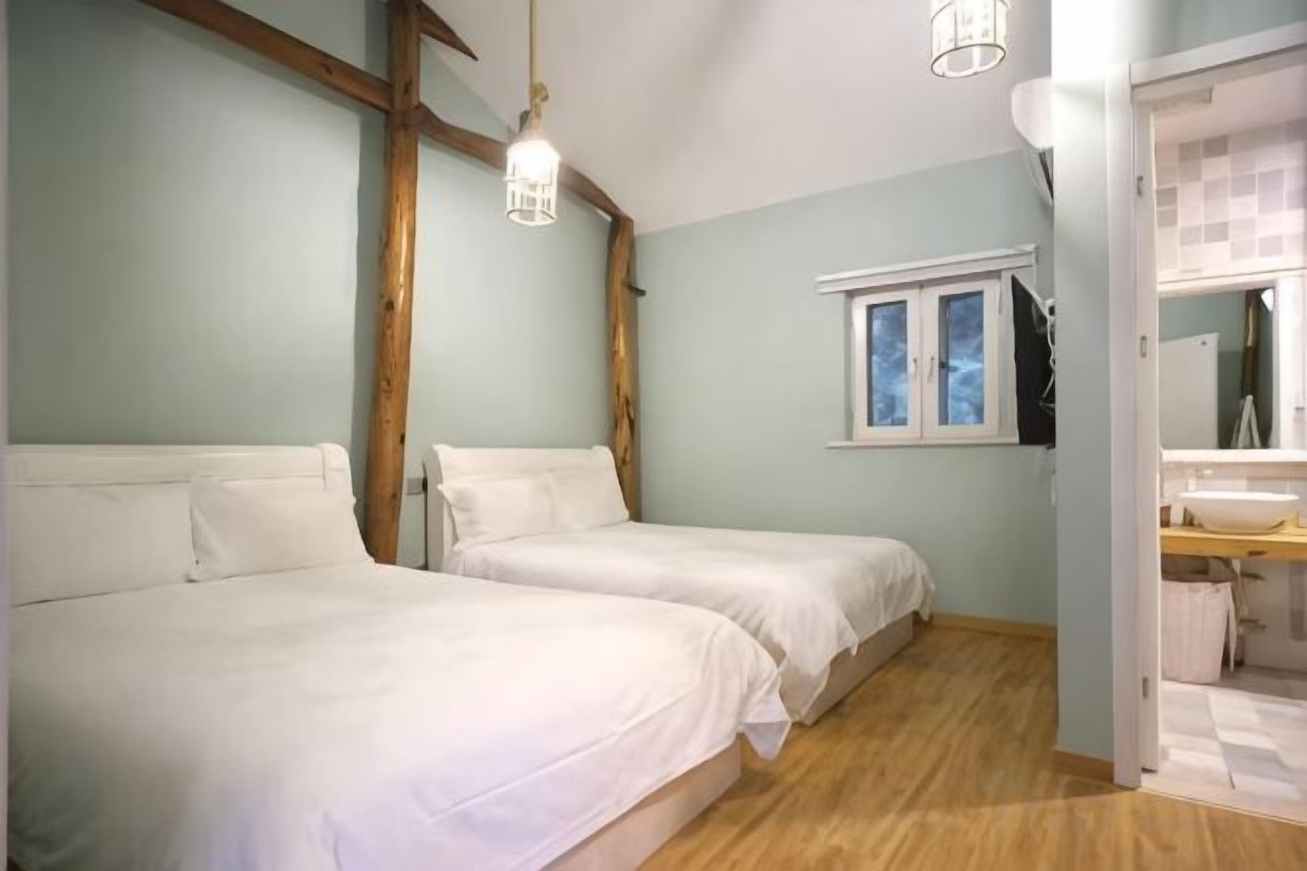 Un dormitorio con dos camas, vigas de madera, una ventana y un baño con espejo y lavamanos.